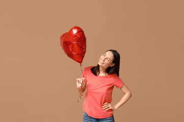 Beautiful young woman with heart-shaped air balloon on beige background