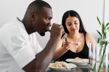 young latin interracial couple, sitting in the dining room eating spaghetti. man serious and angry with his wife.