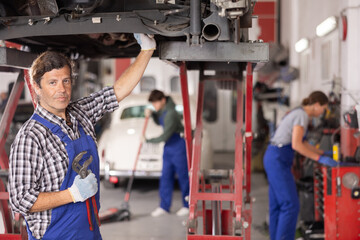 Experienced auto mechanic doing an inspection of rear suspension of a car in a car service center