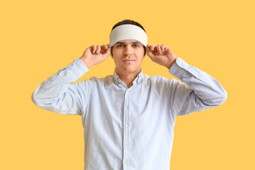 Young man with brain concussion and bandaged head on yellow background