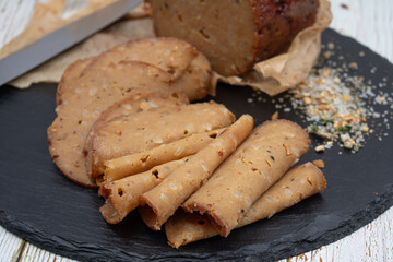Seitan shaped and cooked in ham press, sliced on slate board. Vegan protein, plant based alternative to meat.