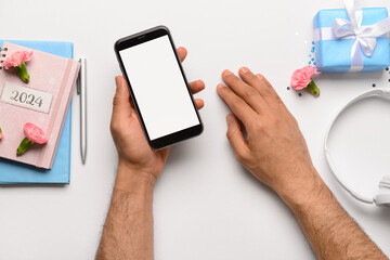 Male hands with modern mobile phone, notebooks and gift box on white background