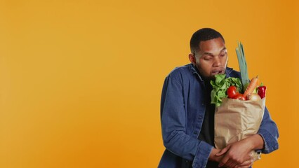 Young adult accidentally dropping an apple from his paper bag full of ethically sourced fruits and veggies, buying a variety of organic homegrown goods. Support vegan lifestyle. Camera B.