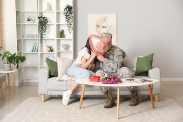 Man in military uniform and his wife kissing behind heart-shaped balloon at home. Valentine's Day...