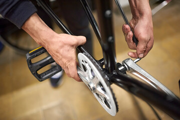 Maintenance service of a bicycle: hands of an unknown repairman assembling the pedals of a bike at...