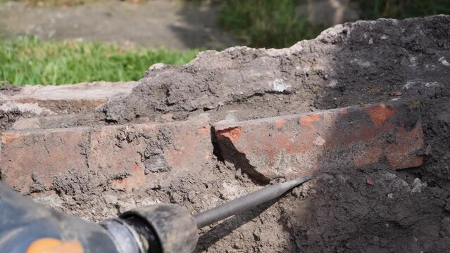 A man using an SDS hammer drill power tool to chisel mortar and bricks out of a concrete block in slow motion