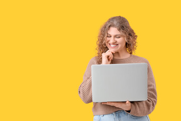 Happy beautiful young woman with laptop on yellow background