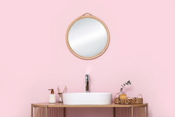 Modern sink with bath supplies on shelving unit near pink wall in bathroom