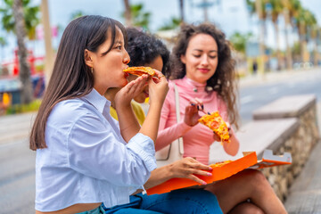 Multi-ethnic women sitting in the city enjoying a pizza together