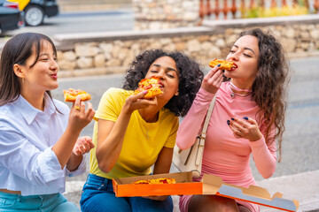 Hungry friends eating take away pizza sitting in the street