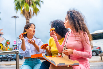 Multi-ethnic friends sharing pizza sitting on street