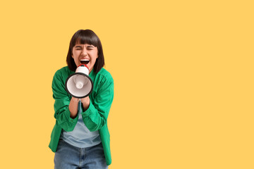 Screaming young woman with megaphone  on yellow background