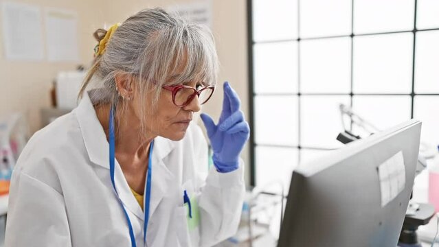Mature woman scientist in lab coat analyzing data on a computer in a laboratory setting.