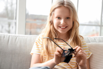 Cute little girl wiping eyeglasses at home