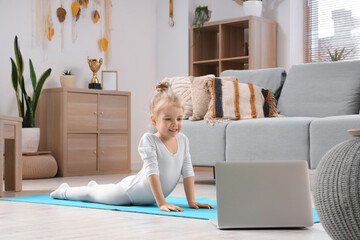 Cute little girl doing gymnastics while watching online tutorial video on laptop at home
