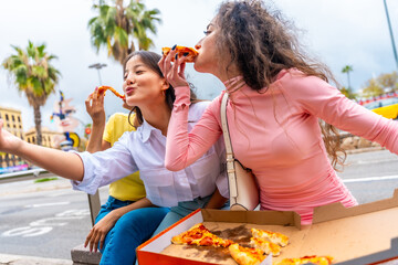 Friends joking while taking selfie eating pizza in the street