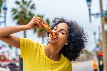 Latin woman enjoying take away pizza in the street