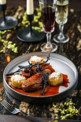 Duck breast meat with potatoes and sauce on plate on marble table with wine glasses. Healthy food, close up, top view