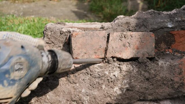 Male construction worker using an SDS impact drill power tool breaker with chisel bit to break bricks and mortar out of a concrete block by hand