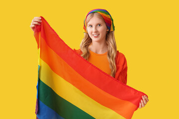 Beautiful young happy woman with LGBT flag on yellow background