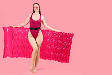 Smiling woman in swimsuit with inflatable mattress on pink background
