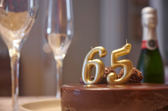 golden 65th birthday candles on a chocolate cake and glasses with champagne during a retirement celebration