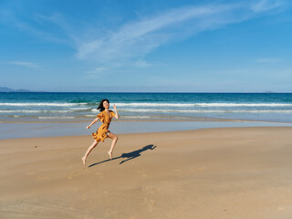 Obraz na płótnie Canvas Happy woman running in yellow dress on sandy beach with clear blue sky background