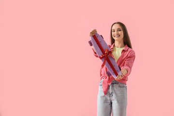 Happy young woman with gift skateboard on pink background