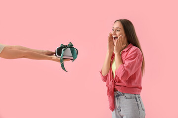 Happy young woman receiving gift VR glasses on pink background