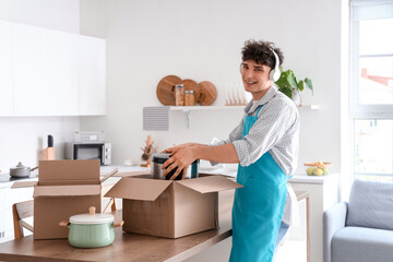 Male janitor with headphones unpacking moving boxes in kitchen