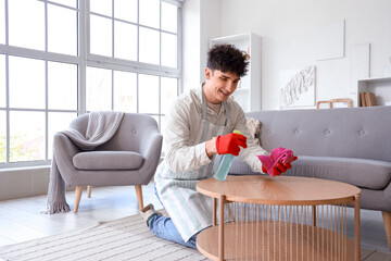 Young man cleaning coffee table at home