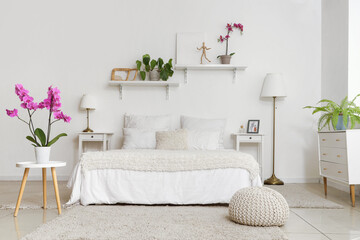 Interior of light room with bed and orchid flower on table