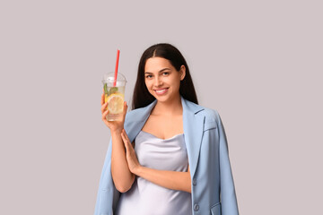 Beautiful young happy woman with cup of fresh lemonade on grey background