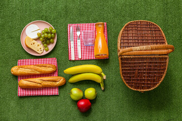 Wicker picnic basket with tasty food and bottle juice on green grass background