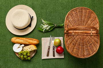 Wicker picnic basket with tasty food, stylish hat and lily-of-the-valley flowers on green grass...