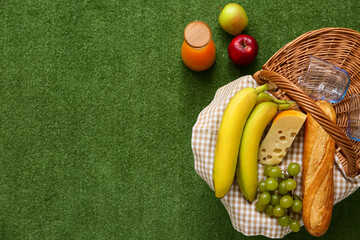 Wicker picnic basket with tasty food, glasses and bottle of juice on green grass background