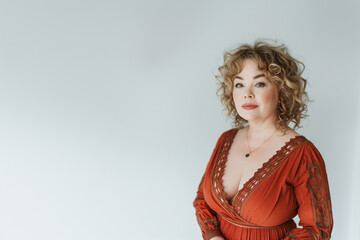 Portrait of a confident mature woman with curly blonde hair, dressed in a luxurious red embroidered dress.