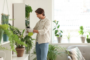 Handsome gardener watering plant on shelf at home