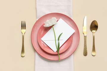 Stylish table setting with beautiful flower and envelope on beige background