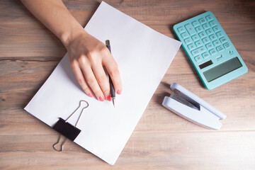 woman hands writing on the paper on a wooden table.