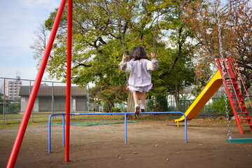 秋の公園でブランコに乗っている小学4年生の女の子の後ろ姿