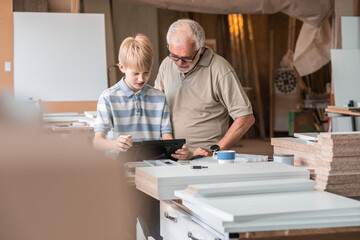 A grandfather teaches his grandson how to fix furniture in his carpenter workshop. They work...