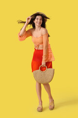 Beautiful young woman with bag and strong wind on yellow background
