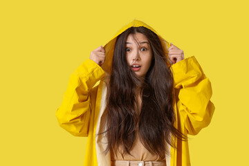 Beautiful Asian woman in raincoat with strong wind on yellow background