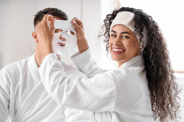 Happy young couple in bathrobes applying facial sheet mask at home