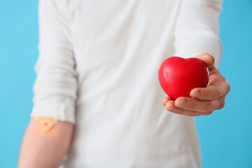 Male blood donor with applied patches and grip ball on blue background, closeup