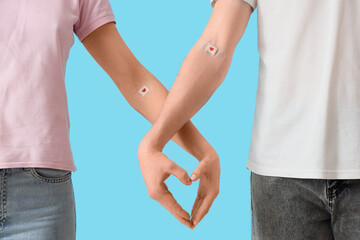 Blood donors with applied patches making heart gesture on blue background, closeup