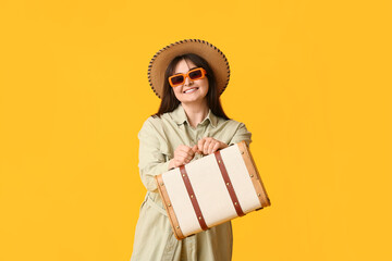 Beautiful young woman with suitcase on yellow background