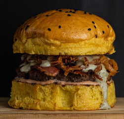 A hamburger with brioche bread with sesame, meat, blue cheese, mustard sauce, slices of bacon and...