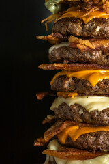 A big pile of burgers with cheddar cheese, mozzarella cheese and slices of bacon in a black background